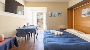 Un dormitorio con cama, escritorio y silla. Hay un televisor montado en la pared y una ventana con vistas al exterior.