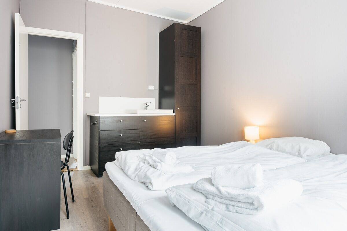 A hotel room with a bed, a desk, a chair, a wardrobe, and a bedside lamp.