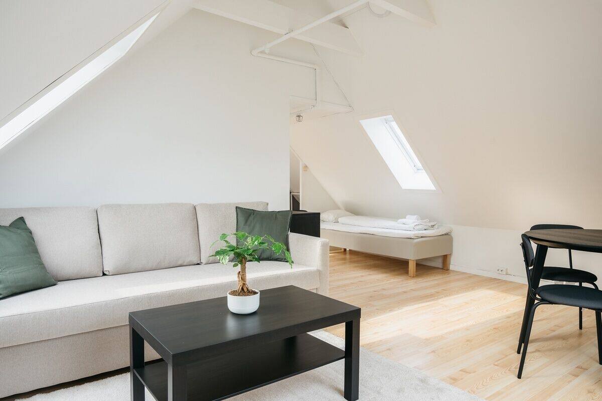 A modern loft apartment with a high ceiling, a skylight, a sofa, a coffee table, a dining table, and a bed.