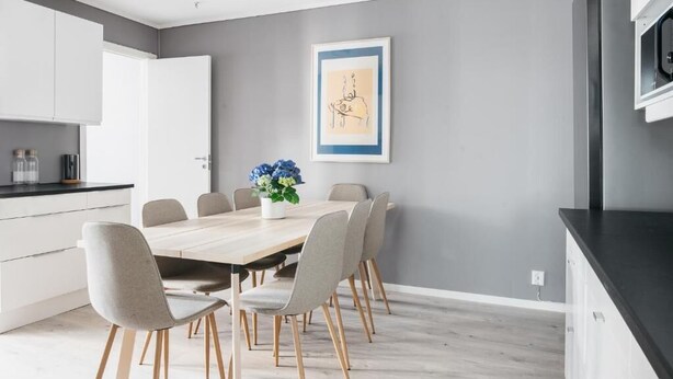 Een moderne keuken met witte kasten, een houten eettafel en grijze stoelen.