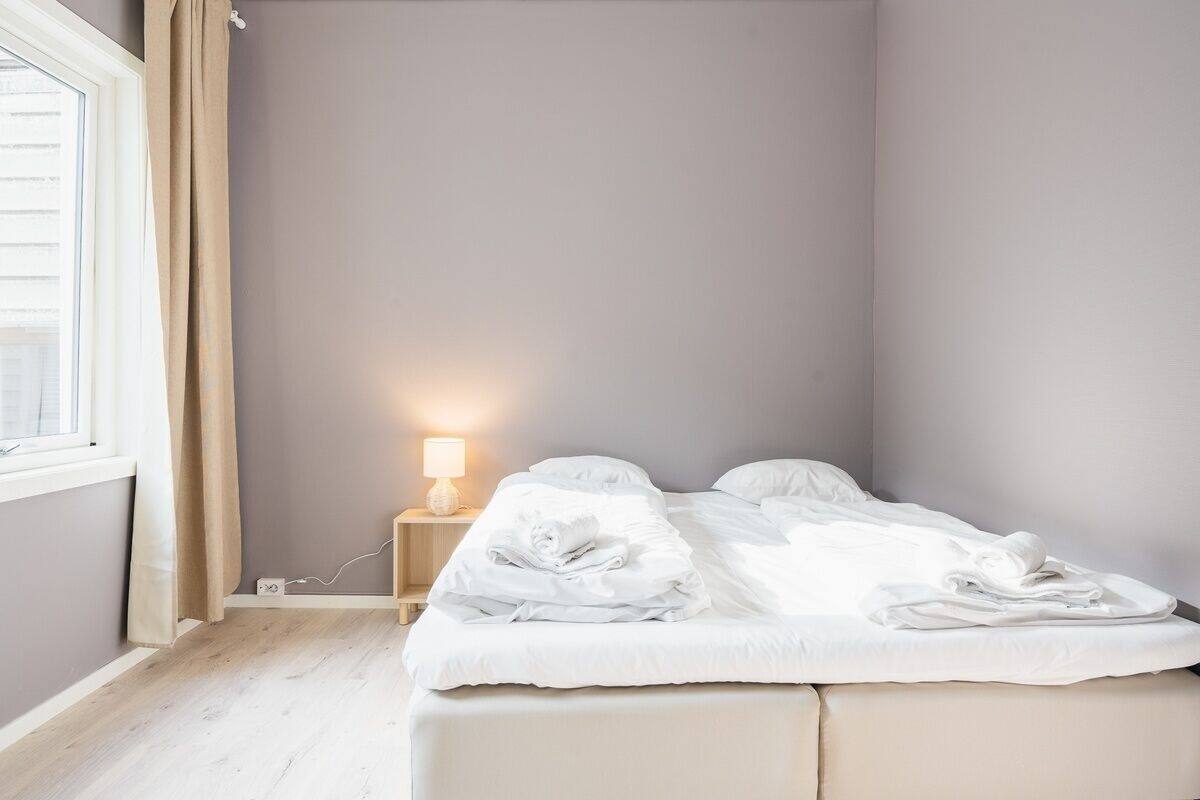 A bedroom with a bed, a nightstand with a lamp, and a window with curtains.
