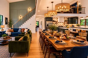 A spacious living area with a dining table set for a meal, a staircase, and a kitchen with dark cabinets. - Luxury 7BR Riverfront-Sleeps Large Groups Hottub (Elkton)