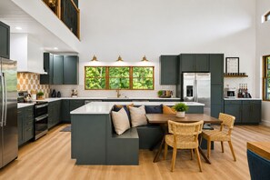 A modern kitchen with dark cabinetry, a central island, and a dining area with wicker chairs. - Luxury 7BR Riverfront-Sleeps Large Groups Hottub (Elkton)