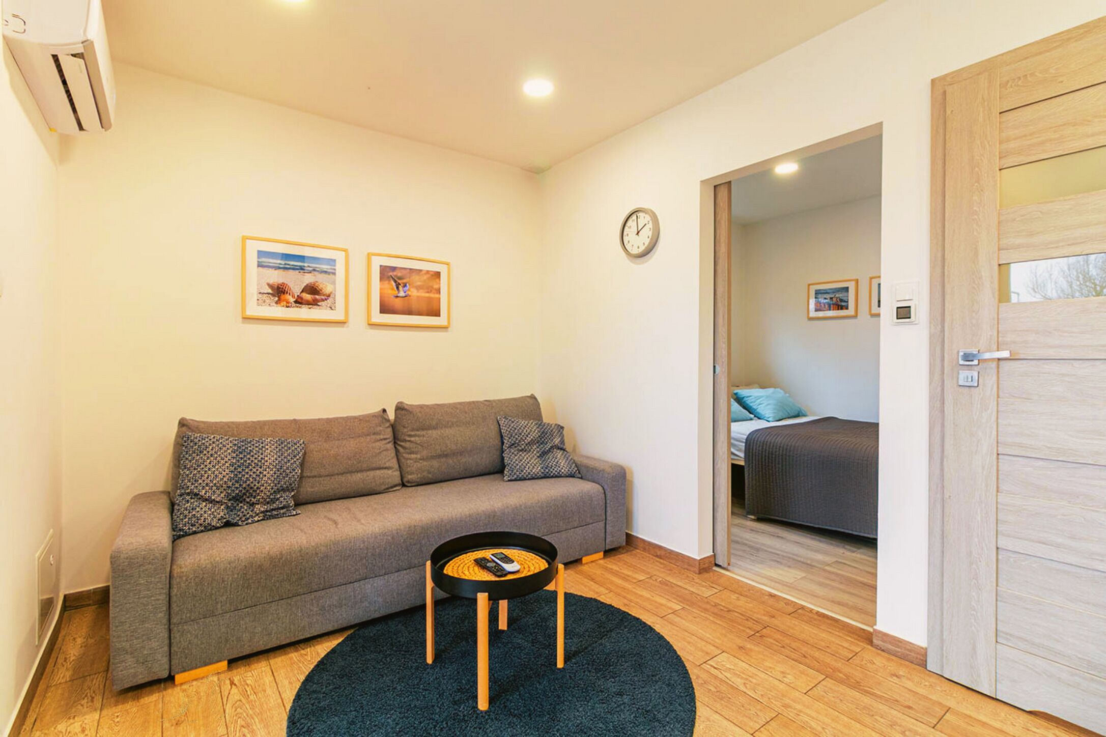 Ein modernes Wohnzimmer mit einem grauen Sofa, einem runden Couchtisch und zwei gerahmten Bildern an der Wand.