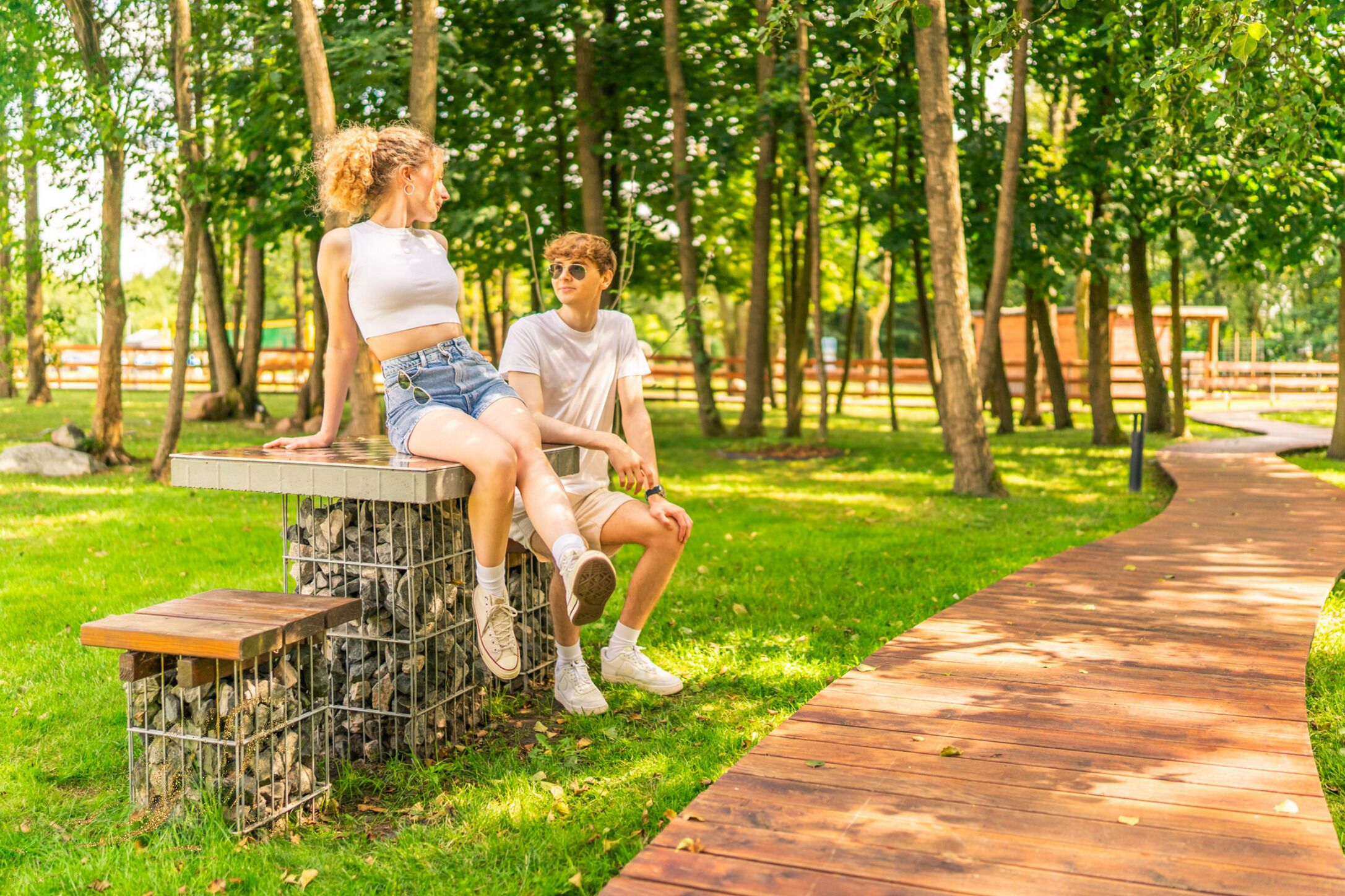 Dos personas sentadas en un banco de piedra en un parque con un sendero de madera.