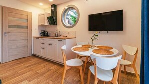 A compact kitchen with a round window, a flat-screen TV, and a dining area with four chairs and a table. - Baltic Natur Park - Family Resort  (Niechorze)