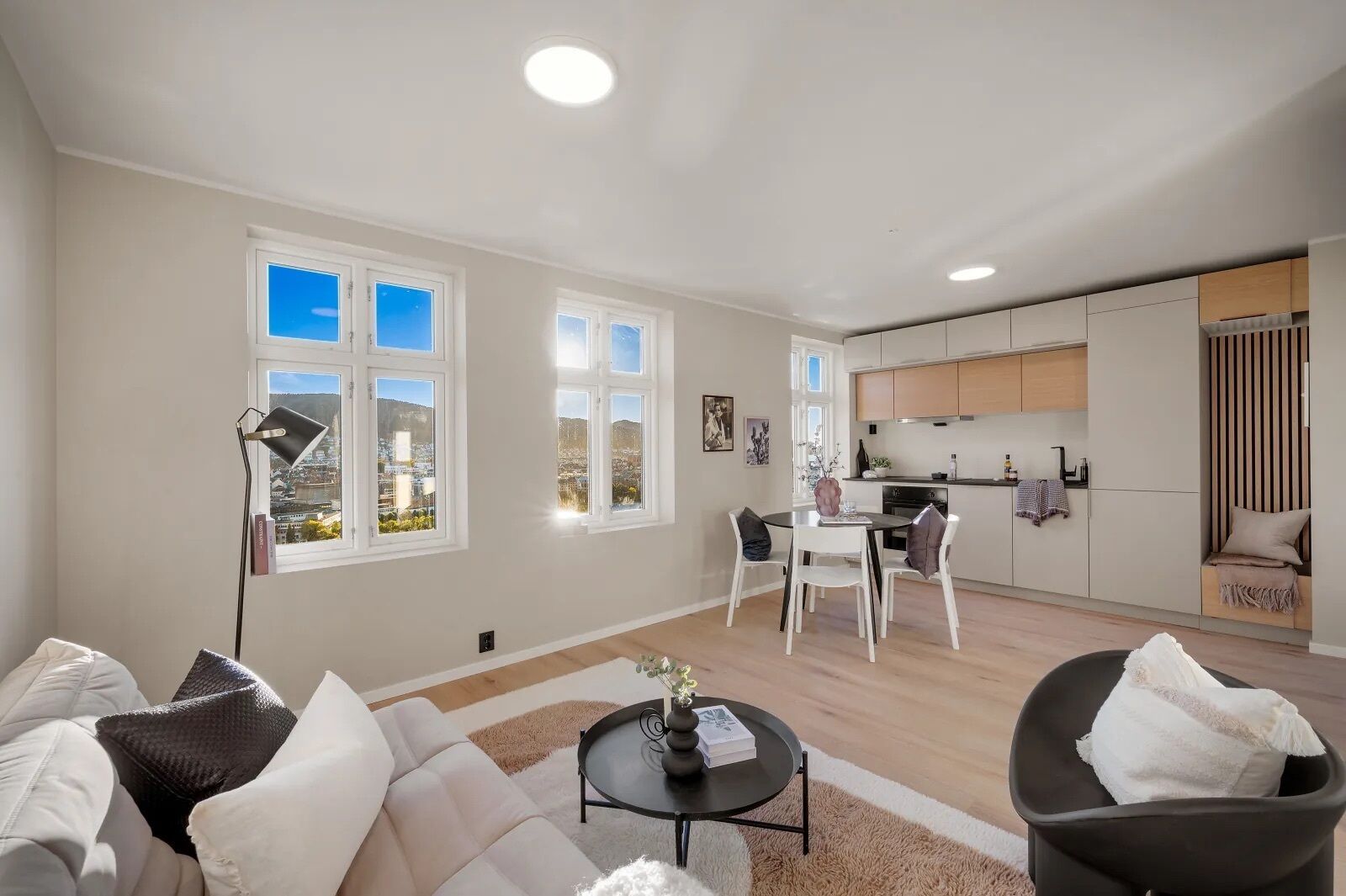 A modern apartment with a living room, dining area, and kitchen. There are large windows providing natural light and a view of the city.