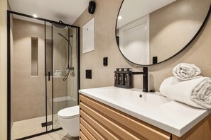Une salle de bain moderne avec une douche à parois de verre, un lavabo blanc et un meuble-lavabo en bois.