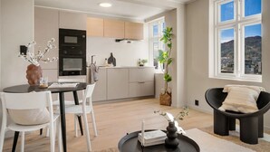 A modern kitchen with white cabinets, a microwave, and a stove. There is a dining area with a table and chairs, and a view of a mountain through large windows.