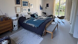 Un dormitorio moderno con una cama grande, mesitas de noche, un aparador, un sillón mecedora y una ventana con cortinas.