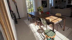 Un comedor con mesa y sillas de madera, una planta en maceta y vistas al exterior a través de una ventana.