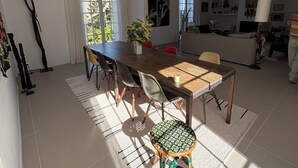 Un salón amplio con mesa de comedor, sillas y sofá. Hay un ventanal grande que proporciona luz natural y un televisor montado en la pared.