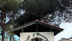 Un sendero de piedra que conduce a un arco blanco con el texto "Golf d'Hossegor" en la parte superior.