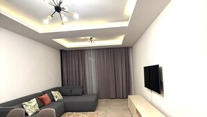 En moderne stue med en modulsofa, et spisebord med stole, et fjernsyn monteret på væggen og en loftlampe.
