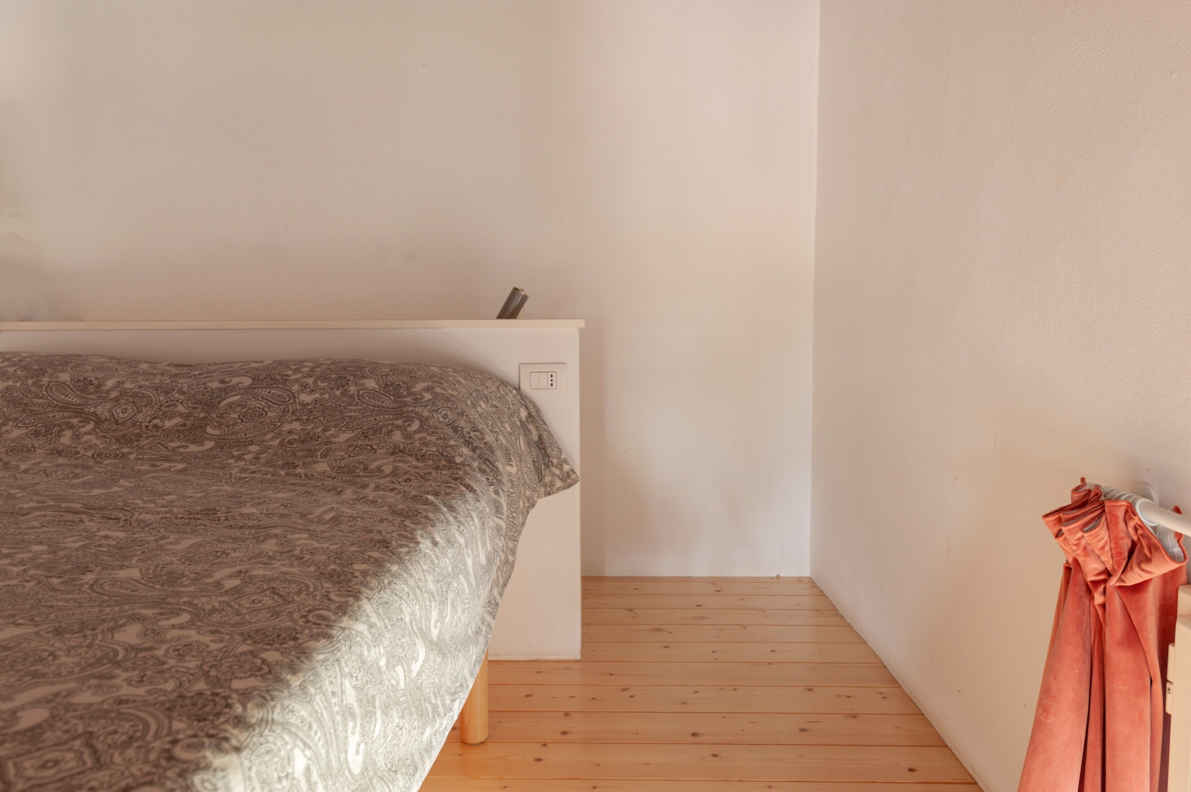 Une chambre à coucher avec un lit, une table de chevet blanche, une prise de courant et un plancher en bois.