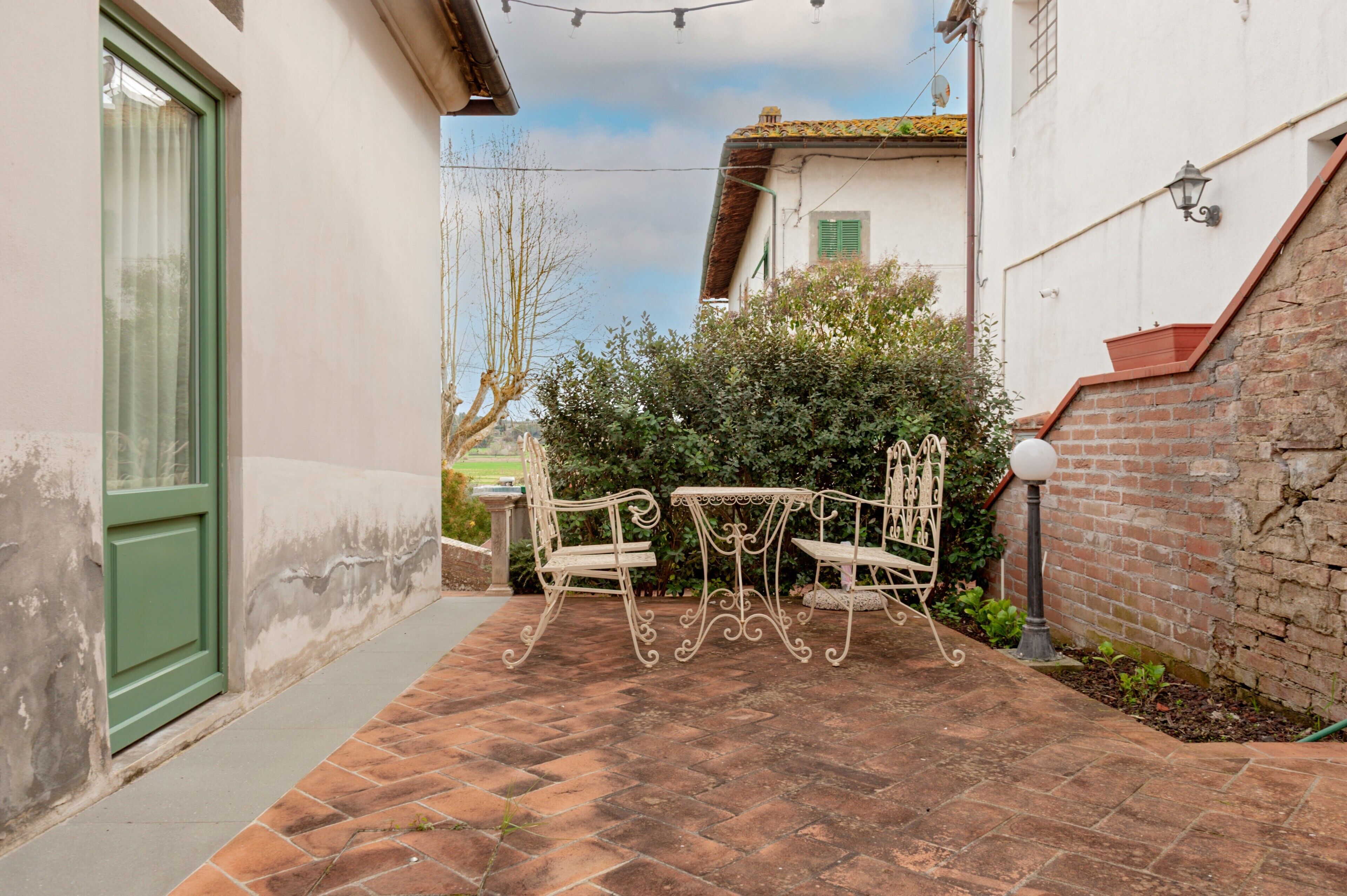 A patio with a table and chairs, a brick wall, and a green door.