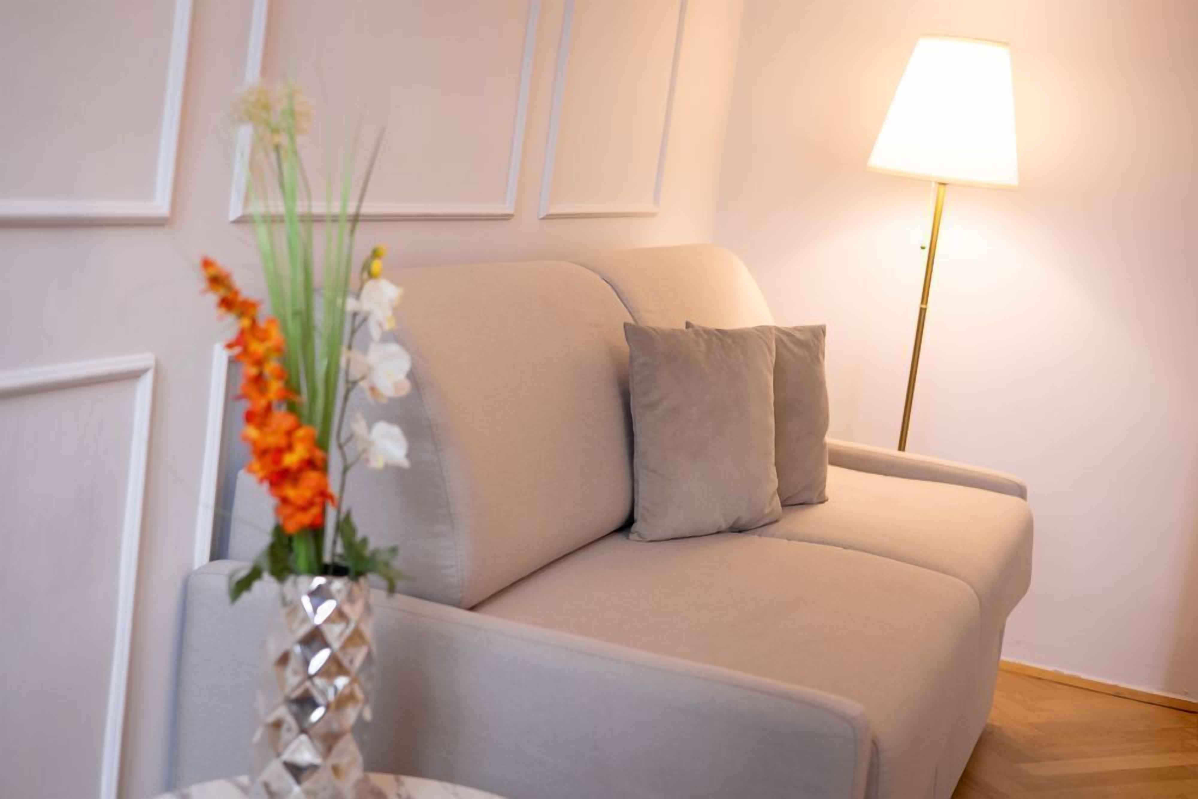 A beige sofa with two pillows, a floor lamp, and a vase with flowers.