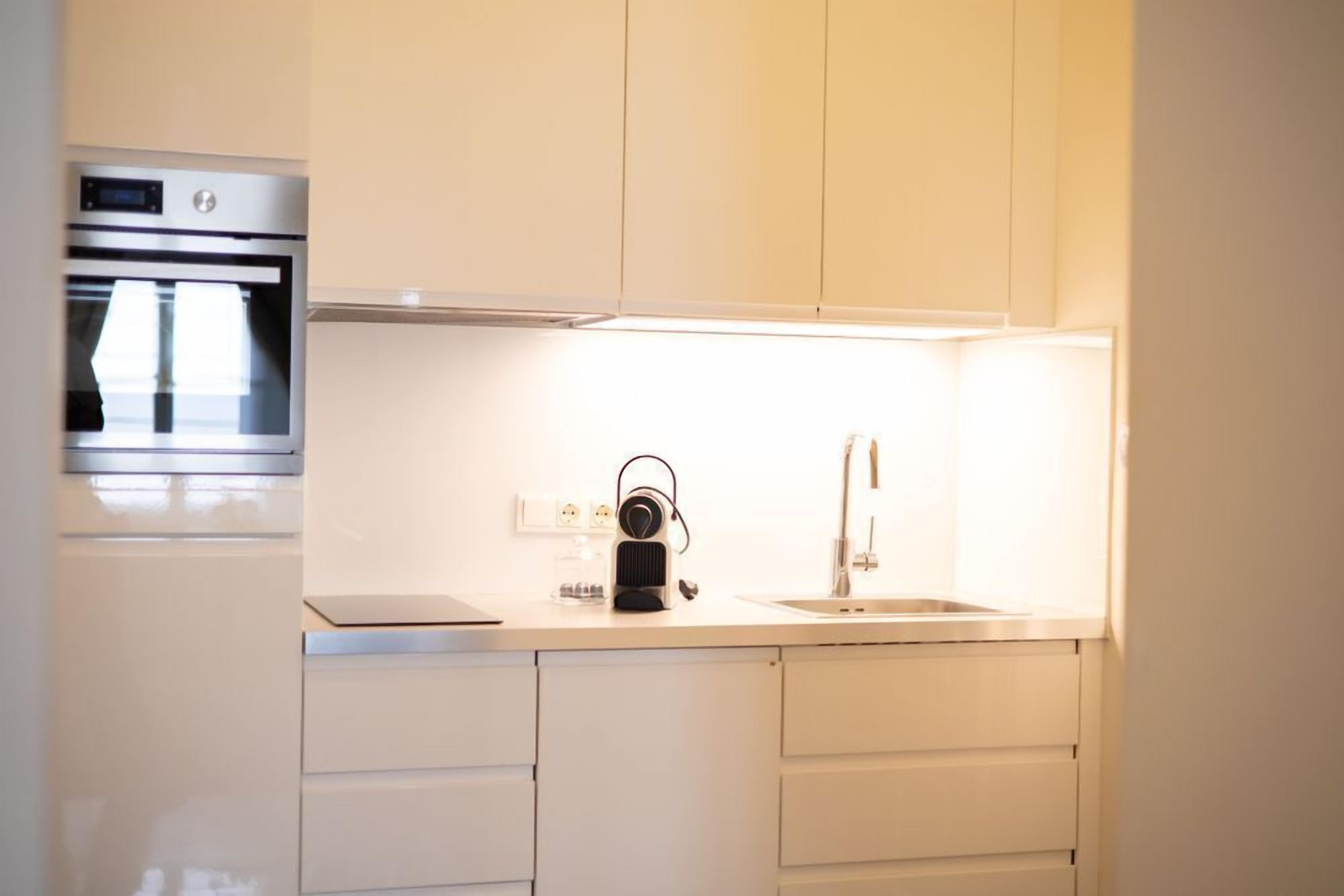 A modern kitchen with white cabinetry, a built-in oven, a sink, and a countertop with a kettle.