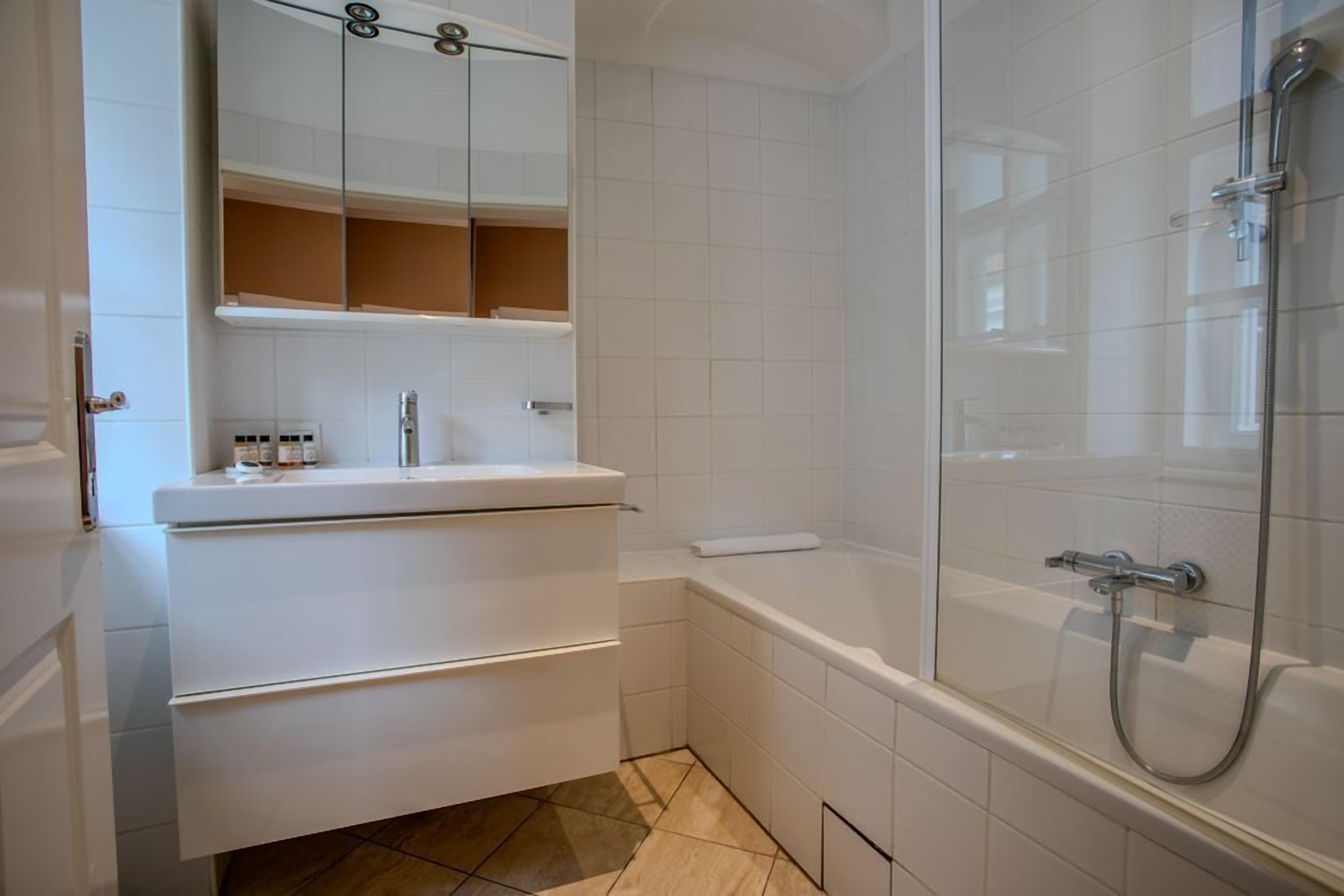 Une salle de bain avec un meuble-lavabo blanc, une baignoire et une douche séparée par une paroi de verre.