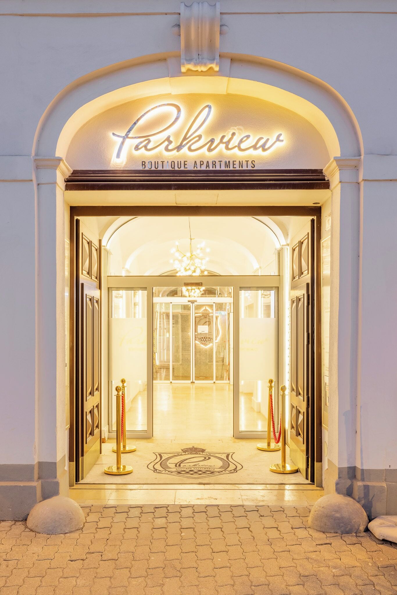 Entrada de un hotel con un letrero de neón que dice 'Parkview Boutique Apartments', un candelabro y una puerta de vidrio.