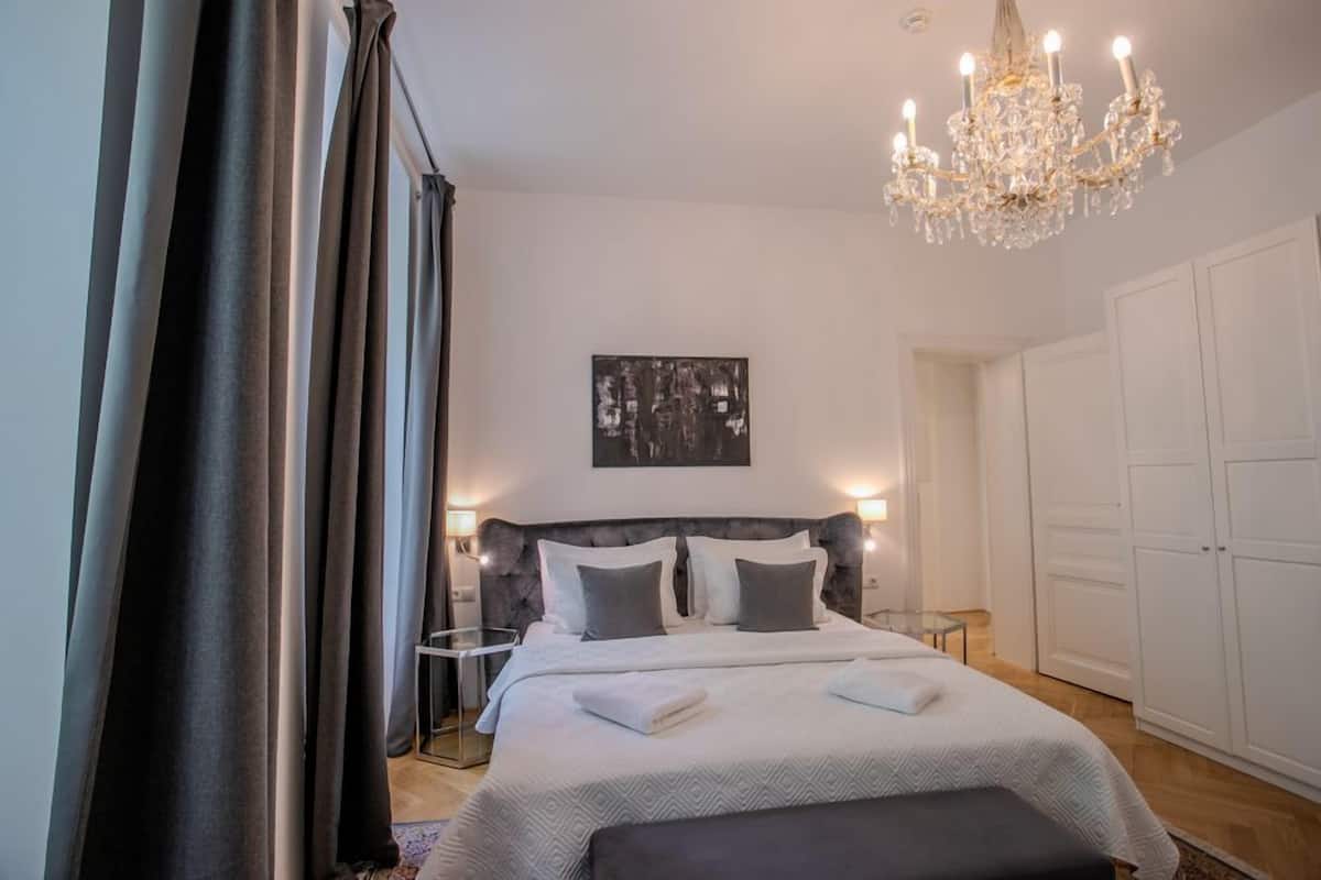 Ein Schlafzimmer mit einem großen Bett, Nachttischen, einer Chandelüster und einem Kleiderschrank.