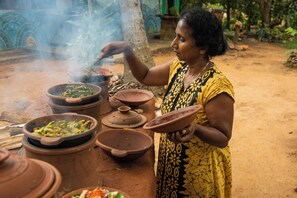A person cooking outdoors with clay pots and a fire. - Jayanti guest house (Sigiriya)