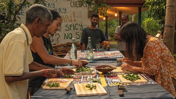 Un grupo de personas preparando comida en una mesa al aire libre con mantel azul, rodeado de vegetación.