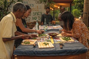 A group of people preparing food at an outdoor table with a blue tablecloth, surrounded by greenery. - Jayanti guest house (Sigiriya)