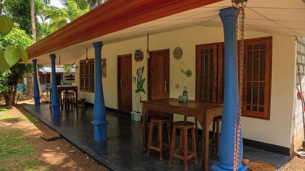 A covered outdoor area with wooden tables and blue pillars, a dining table with stools, and a potted plant. - Jayanti guest house (Sigiriya)