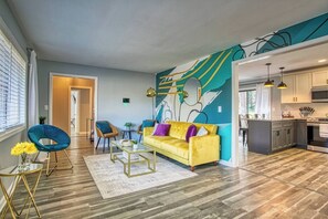 Un salon moderne avec un canapé jaune, un fauteuil bleu et une fresque murale abstraite aux couleurs vives.