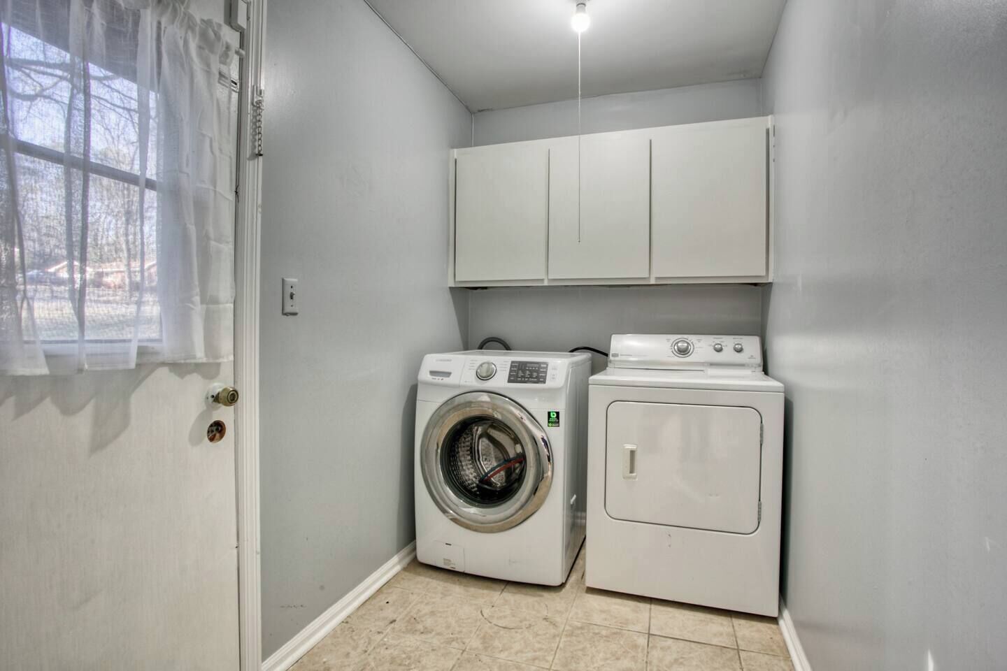 Une buanderie équipée d’un lave-linge et d’un sèche-linge, une porte avec une fenêtre et un luminaire au plafond.