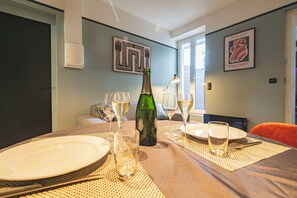 Una mesa de comedor dispuesta con platos, vasos y una botella de vino, con un sofá y una silla al fondo.