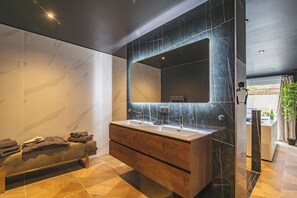 Un baño moderno con un espejo grande, dos lavamanos, un tocador de madera y un banco con toallas.