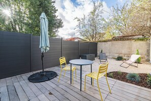 Un patio con una mesa redonda y cuatro sillas, una sombrilla y una pequeña zona ajardinada con plantas y un cactus.