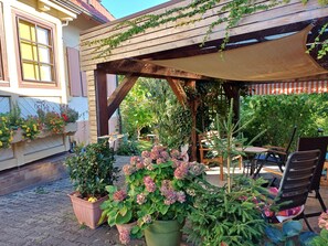 A covered outdoor seating area with wooden beams, potted plants, and a table with chairs.