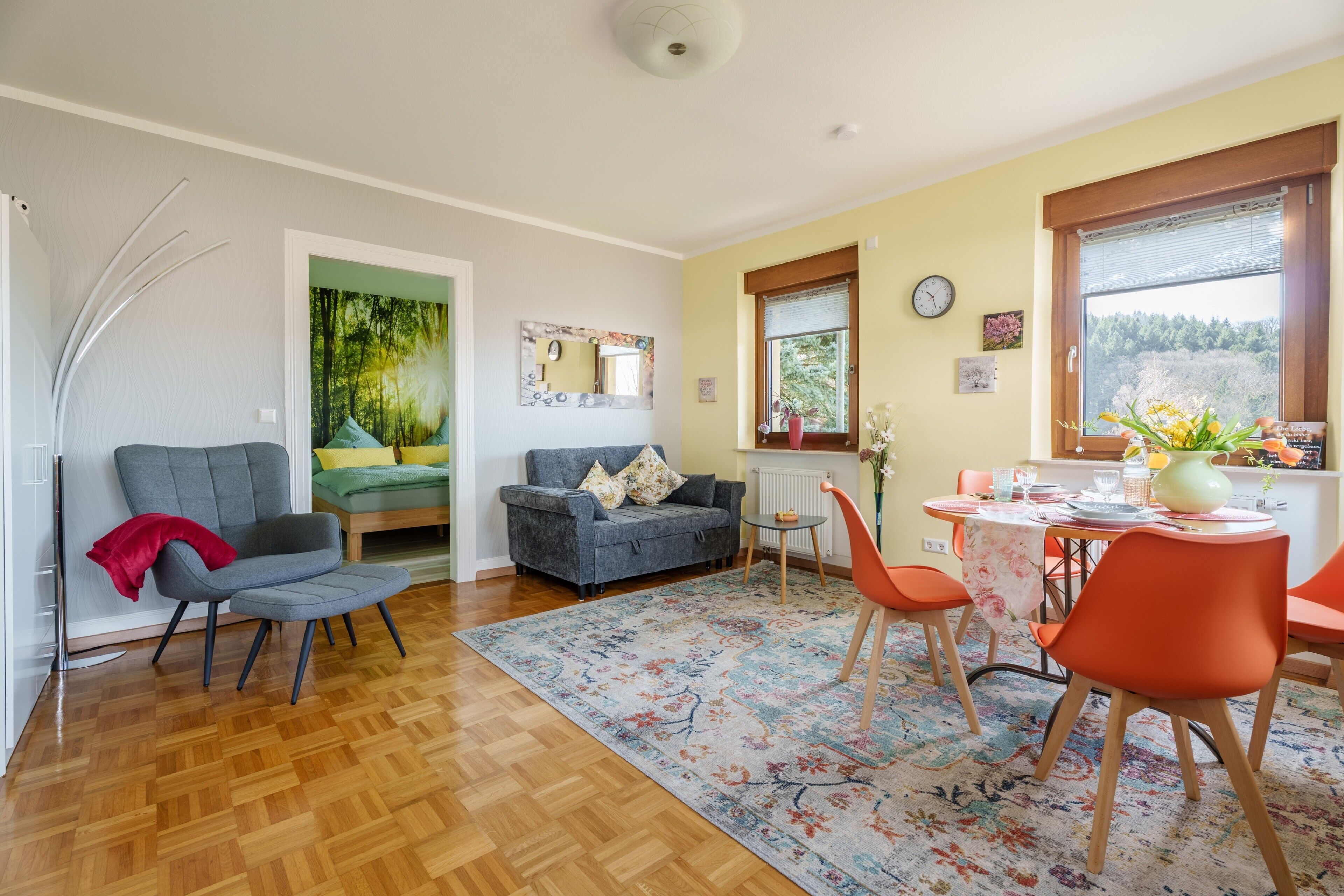 A modern living room with a sofa, a dining table with chairs, a rug, and a window with a view.