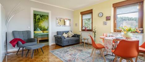 A modern living room with a sofa, a dining table with chairs, a rug, and a window with a view.