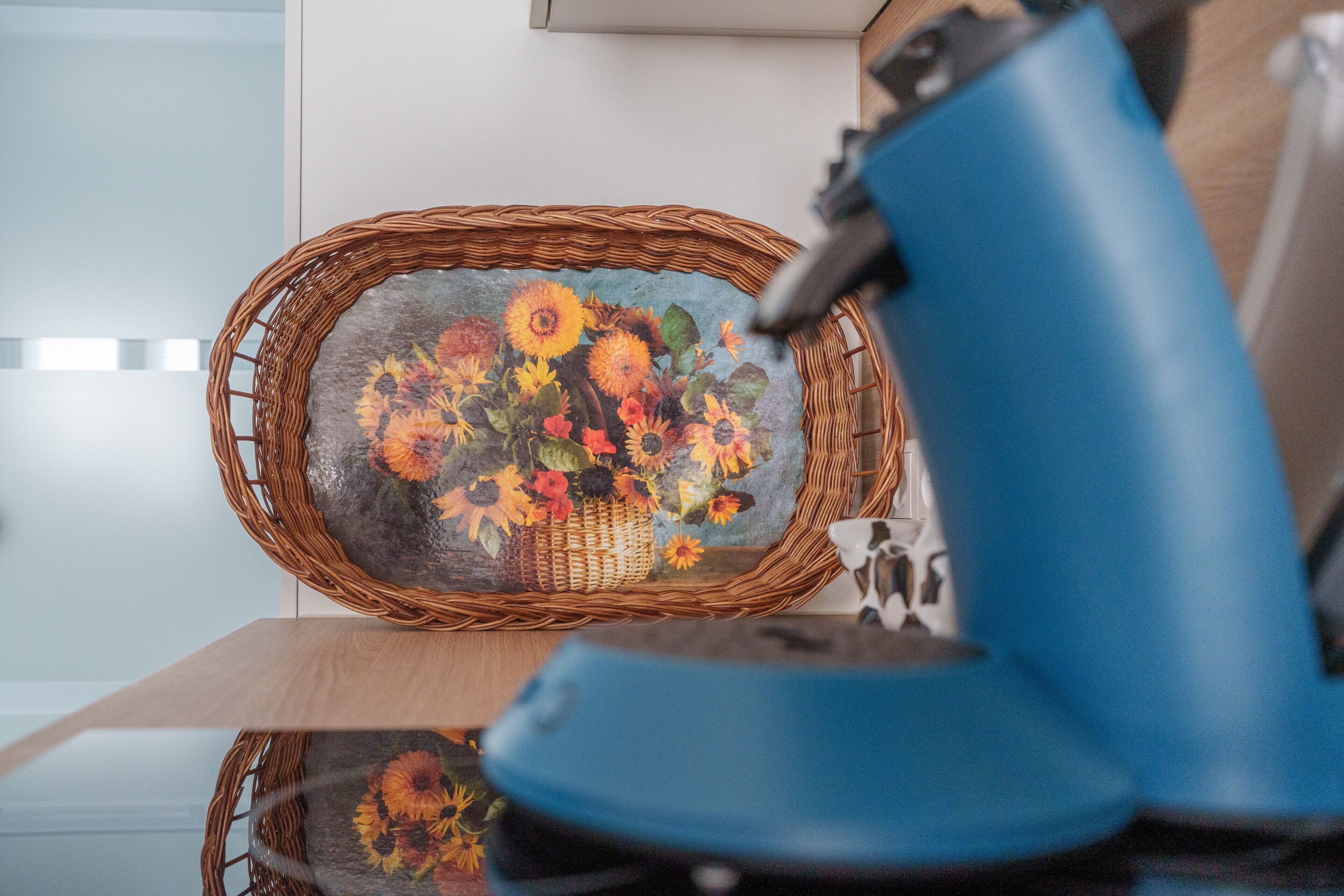 Un panier en osier orné de motifs floraux, une lampe bleue et une table en bois.