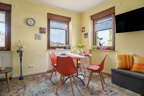 Ein Essbereich mit einem Tisch für vier Personen, umgeben von orangefarbenen Stühlen, einer Vase mit Blumen und einer Uhr an der Wand.