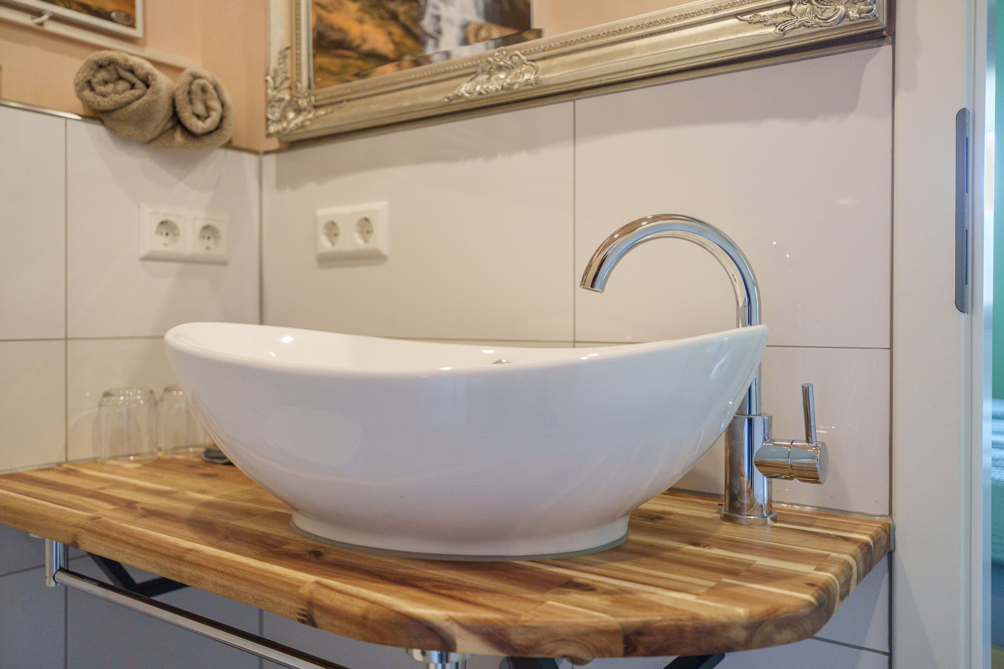 A white vessel sink with a chrome faucet on a wooden countertop in a bathroom.