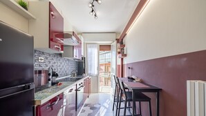 Una cocina estrecha con un refrigerador negro, un salpicadero de azulejos y una zona de comedor con mesa y sillas.