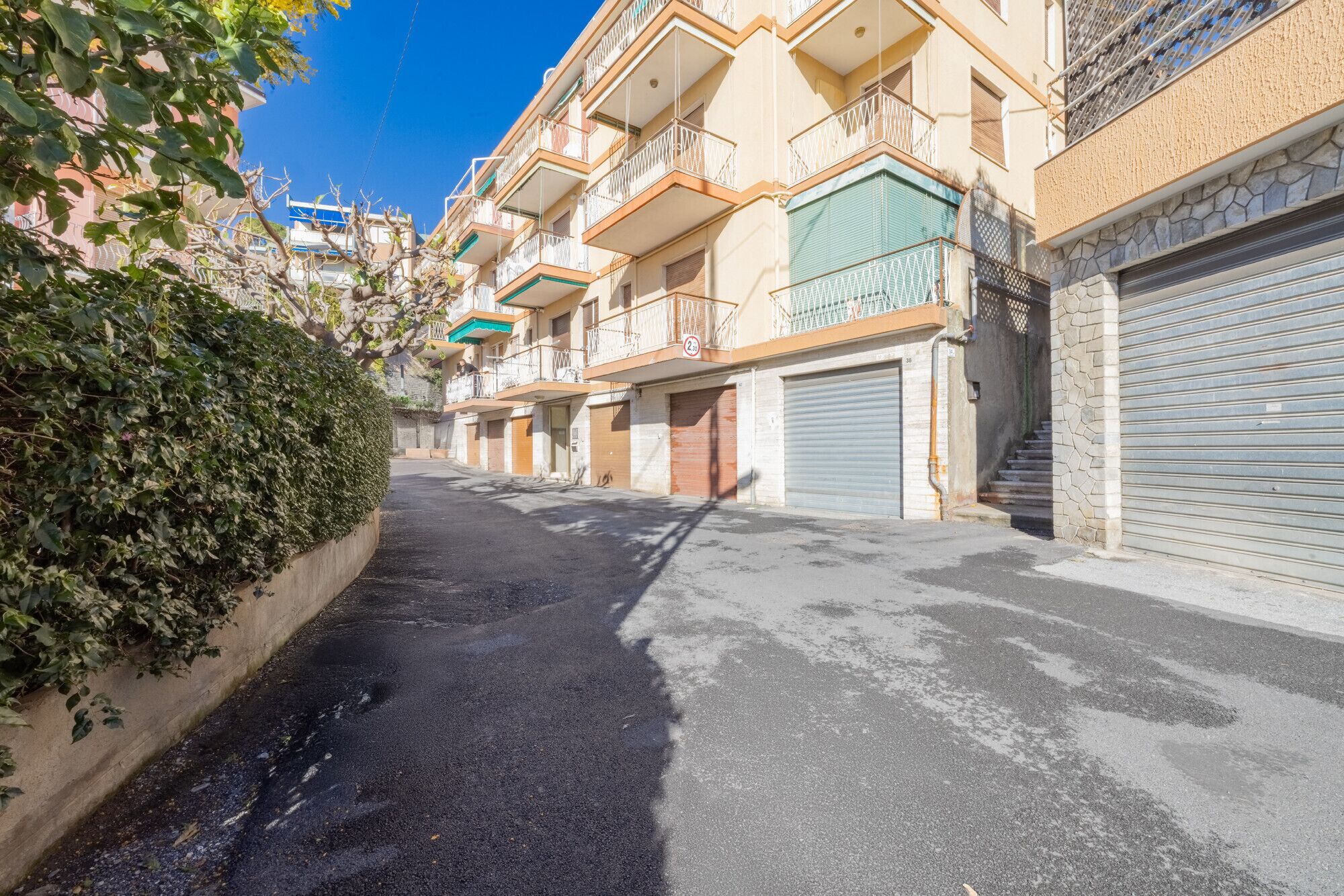 Une rue étroite, bordée de bâtiments des deux côtés, avec des balcons et une enseigne bien visible indiquant une limite de hauteur.