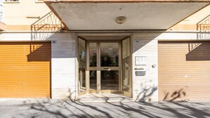 Entrada de un edificio con puerta de cristal, reja de metal y suelo de hormigón.