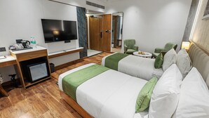 Habitación de hotel con dos camas, un escritorio con ordenador, televisor de pantalla plana, espejo y sillón verde.
