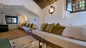 Una habitació acollidora amb un sofà blanc, una banca de fusta i una taula petita amb una ampolla i un got.