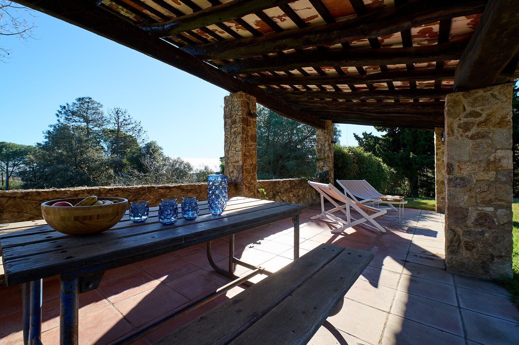 An outdoor patio with a wooden table, chairs, and a stone wall.