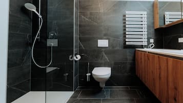 A modern bathroom with a glass-enclosed shower, a toilet, and a wooden vanity.