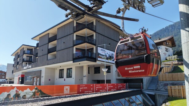 A modern building with balconies, a ski lift, and a sign for 'Hansi Hinterseer.' - KitzSki Living (Kitzbühel)