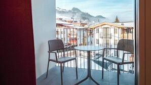 A balcony with two chairs and a table, overlooking a mountainous area with buildings and a ski lift. - KitzSki Living (Kitzbühel)