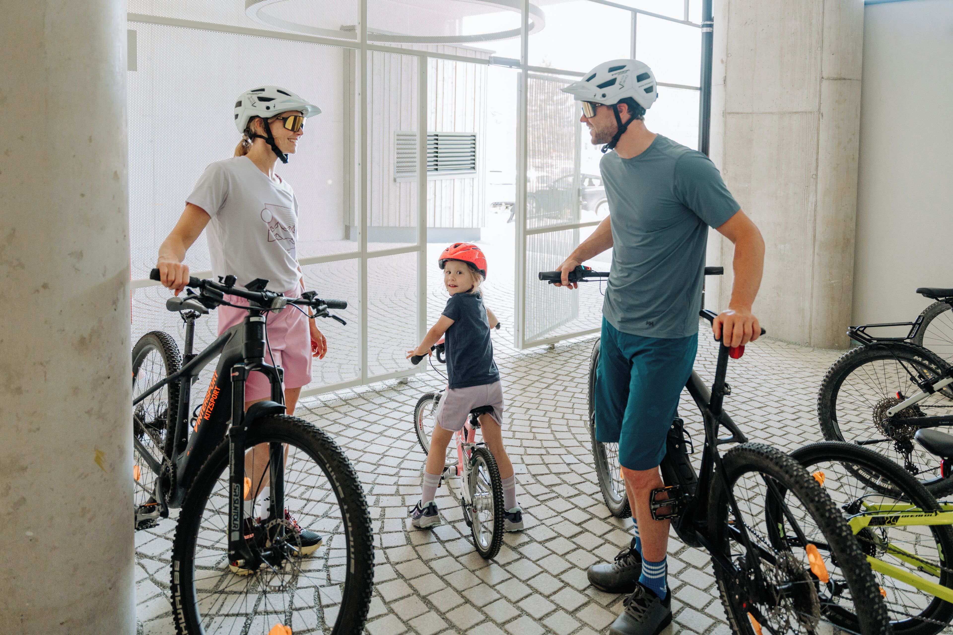 A group of people with bicycles inside a building with a tiled floor and large windows.
